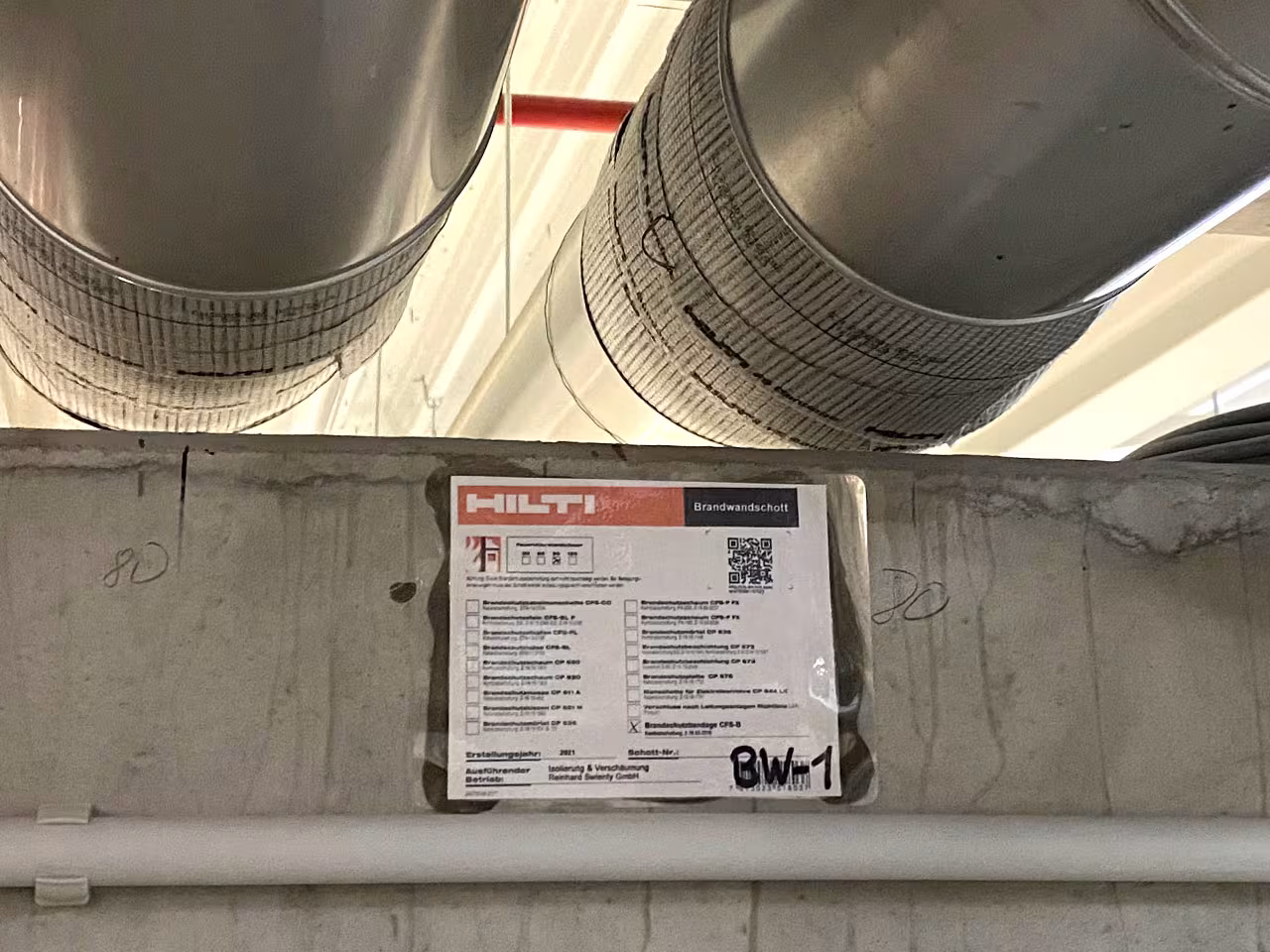 Brandschutzisolierung mit Hilti Brandwandschott CFS-B an Lüftungsrohren — Brandwanddurchführung mit Kennzeichnungsschild BW-1