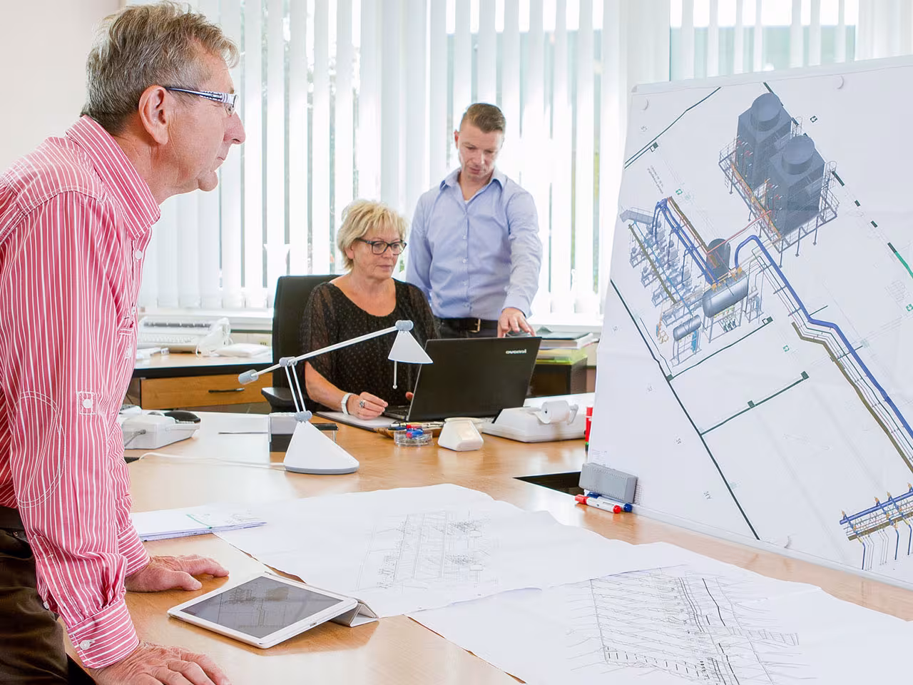 Projektplanung und Projektbegleitung im Büro — Ingenieure besprechen Isolierungsplanung mit Anlagenzeichnungen und Dämmdickenberechnung